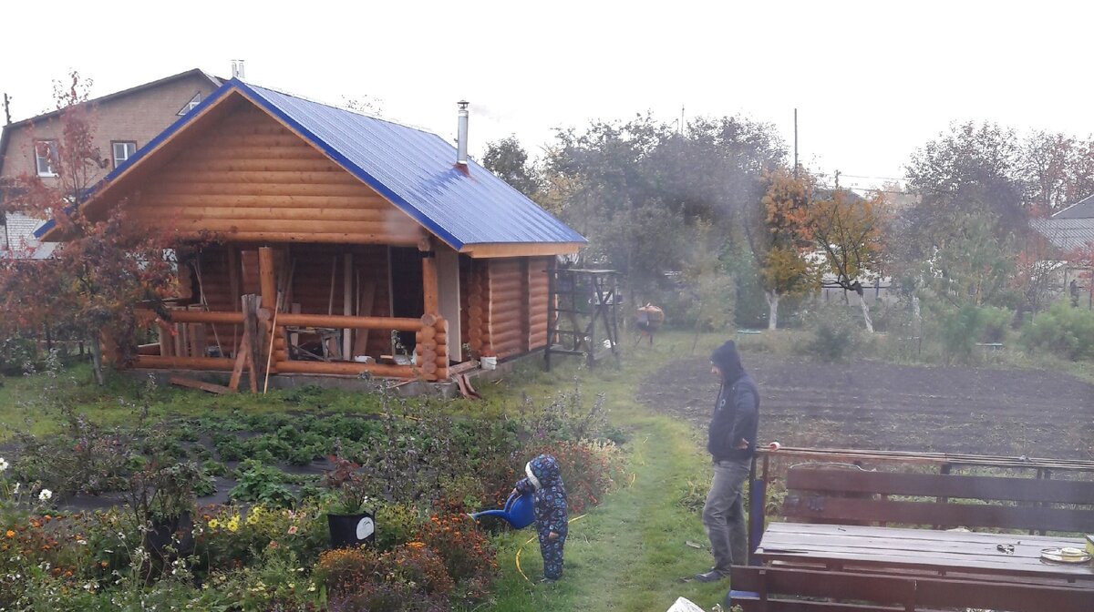 Фото автора. Вот наша баня, еще в процессе стройки, но уже пробуем топить. Миша поливает увядшие цветы. Октябрь 2019