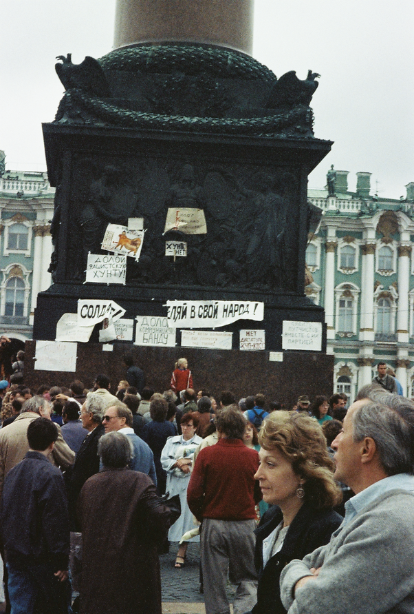 Протестующие на Дворцовой площади с транспарантами и плакатами, приклеенными к Александровской колонне.