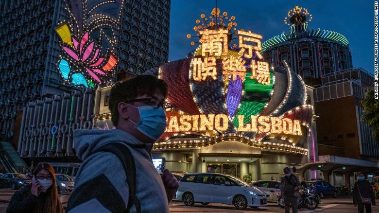 Люди в масках на лицах проходят перед отелем Grand Lisboa 28 января 2020 года в Макао.
