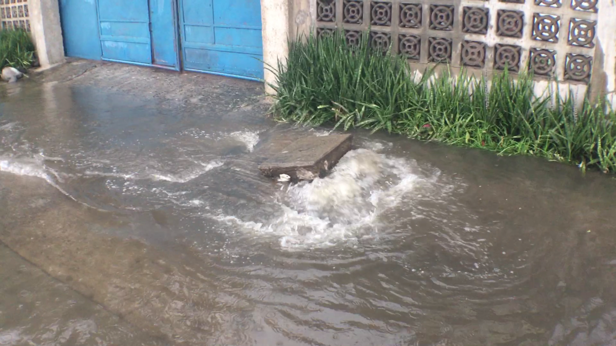 Вода не уходит, а наоборот — бьет фонтаном из под тротуара. Там скрыты канализации.