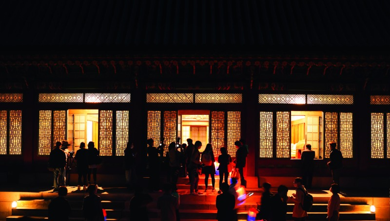 Участники программы «Прогулка под луной в Чандок-куне» перед зданием Тэчжо-чжон. Запущенная в 2010 г. Администрацией культурного наследия и Корейским фондом культурного наследия, эта программа, позволяет осмотреть зоны, обычно закрытые для публики, и поэтому она пользуется большой популярностью. © Joongang Ilbo