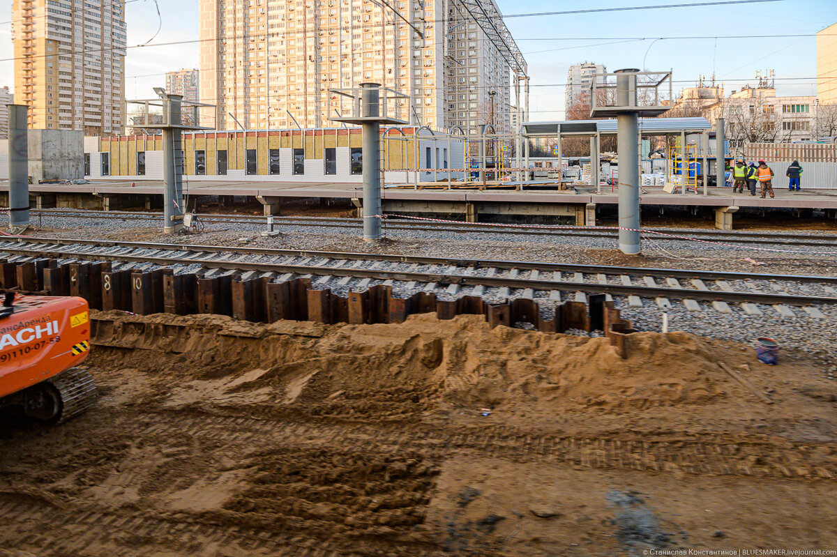 
На перегоне от станции Фили до станции Кунцевская в скором времени должна появится еще одна станция. На самом деле в этом есть смысл. Железнодорожные пути проходят практически в нескольких метрах от выхода со станции метро "Славянский бульвар" и не сделать тут остановочный пункт было бы опрометчиво. К тому же пересадка со станции МЦД "Кунцевская" на одноименную станцию метро совершенно не удобная. Поэтому логично было построить остановку здесь, около "Славянского бульвара", чтобы пассажиры пересаживались на "синюю" ветку именно тут. Еще один интересный момент, станцию решили делать по оригинальному проекту, тут не стали делать станционный комплекс над путями с конкорсом и спусками на платформу, хотя ничего этому не мешало. Вместо этого мы получим станцию с подземным расположением вестибюлей, а также с огромной накрывашкой, которая накроет все платформы, что по похожее мы видели на станции МЦК "Лужники". Итак, станция "Славянский бульвар" сейчас находится в процессе строительства и можно посмотреть, как в чистом поле появляется новый комплекс, заодно посмотрим рендеры, чтобы не возвращаться к ним, когда станция будет уже готова.