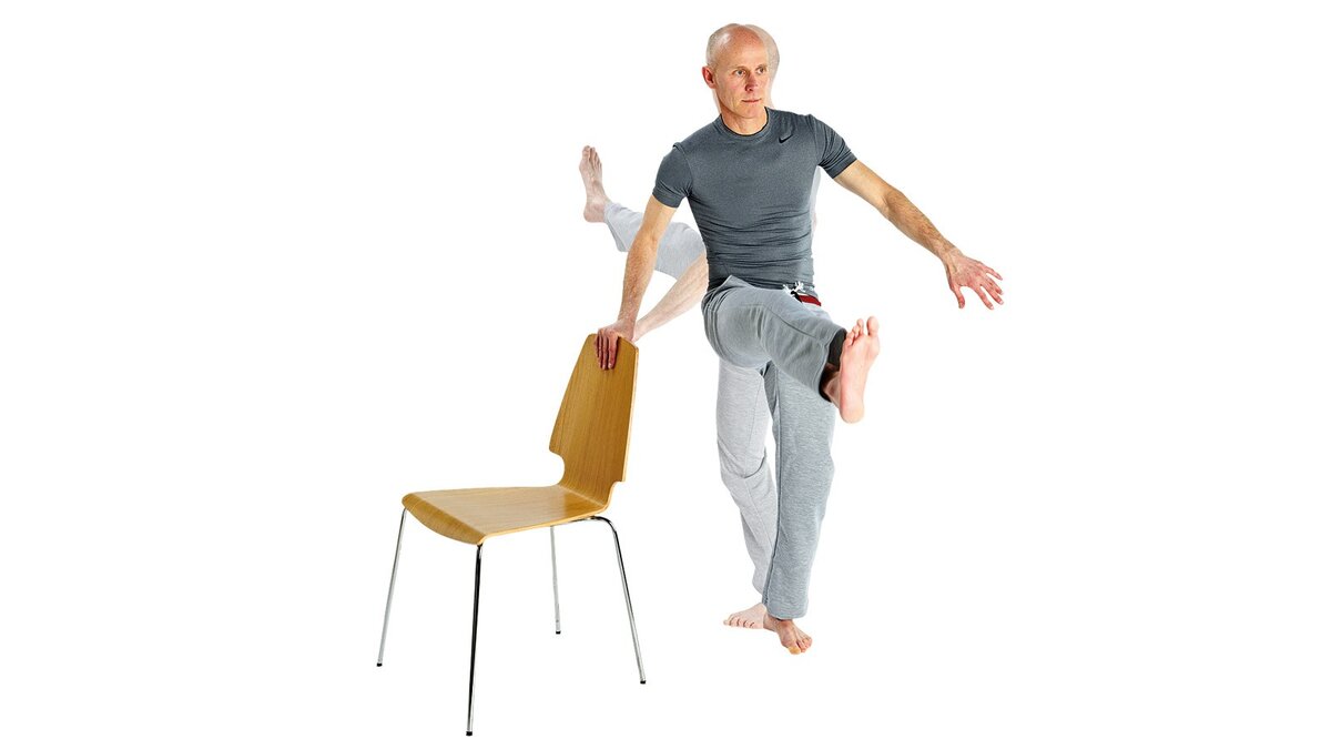 Сядь постой. Мужик со стулом в руках. Ноги на стуле. Стул для вставания ногами. Человек поднимает стул.