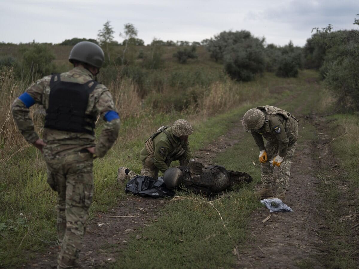    Украинские военнослужащие осматривают тело солдата в Харьковской области, 17 сентября 2022 г.© AP Photo / Leo Correa