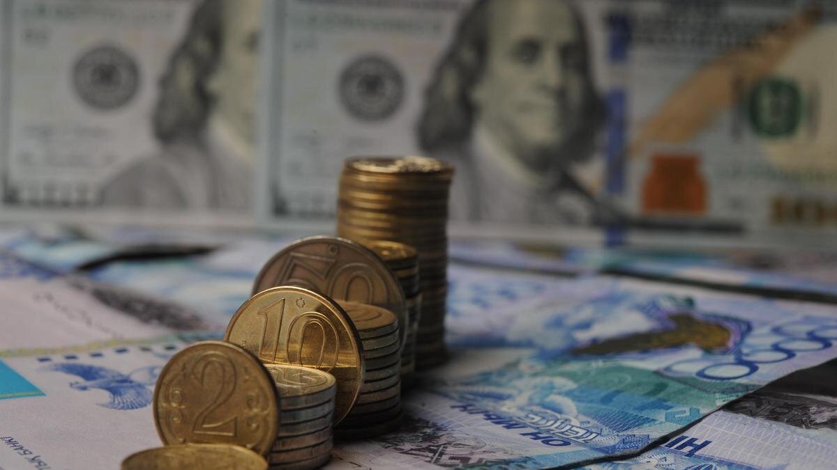    Стопки монет тенге стоят на фоне купюры доллара:NUR.KZ/Владимир Третьяков