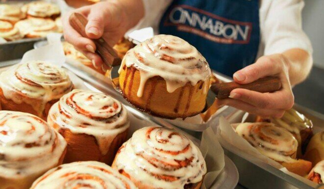 Cinnabon - известная сеть кафе по всему миру, которая радует своих посетителей вкуснейшими десертами и свежей выпечкой. Самое известное блюдо их пекарни - булочки с корицей, покрытые нежнейшим сливочным кремом. На первый взгляд может показаться, что это обычные дрожжевые булочки с корицей. Однако попробовав раз, очень сложно остановиться, чтобы не съесть все и сразу. Секрет заключается в креме, который пропитывает выпечку и в сочетании с корицей делает ее необычайно нежной. Но мало кто знает, что эти булочки можно приготовить в домашних условиях и получаются они ничуть не хуже оригинала!
