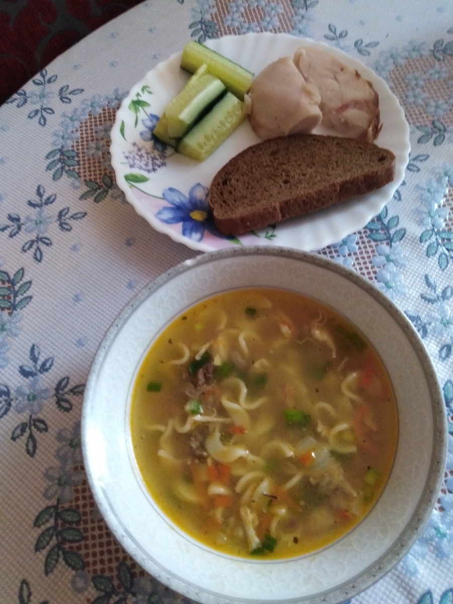 суп с лапшой ,кусочек темного хлеба,небольшой кусочек мяса и огурец.