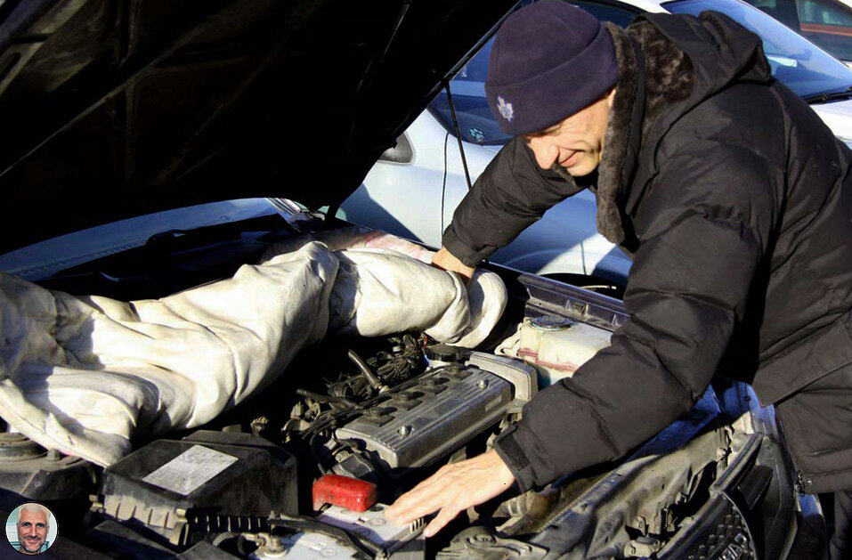Автолюбитель осматривает  замерзший двигатель и аккумулятор. Пытается произвести пуск замерзшего двигателя