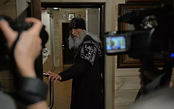 "Я не уйду отсюда. Пусть приезжает полиция и Росгвардия за мной! Монастырь придется брать штурмом!" — запинаясь, произносит схиигумен Сергий на камеру.В его руках текст обращения "к верующим и общественности". В последнюю неделю монах зачитывает такие послания ежедневно. И Среднеуральский женский монастырь, где он был духовником 18 лет, оказался в центре скандала.Последний виток начался 16 июня — с сообщений местных СМИ о том, что обитель окружили казаки, не позволяющие никому войти внутрь. Затем появилась информация, что отец Сергий выгнал за монастырские ворота настоятельницу — игуменью Варвару (Крыгину). Назначенного же епархией нового духовника обители туда попросту не пустили.Три недели назад, 27 мая, Екатеринбургская епархия запретила отца Сергия в служении. Месяцем ранее ему запретили проповедовать. А закрутилась вся эта история, когда по Сети разлетелся видеоролик с обращением схиигумена в храме после службы. В своей проповеди он проклял тех, кто закрывает церкви из-за пандемии COVID-19. Саму болезнь монах считает выдуманной, называя "якобы коронавирусом", а смерти от нее среди духовенства (около двух десятков человек) объясняет "массовым неверием".© РИА Новости / Павел ЛисицынПерейти в фотобанкСхиигумен Сергий в Среднеуральском женском монастыре в Свердловской областиРешения епархии отец Сергий не принял и продолжил проповедовать и служить. Его судьба должна была решиться 15 июня на церковном суде, однако непокорный схимник досрочно покинул заседание. Разбирательство, как и положено по уставу РПЦ, проходило в закрытом режиме, однако выступление схиигумена на нем разошлось по Сети.Новое слушание назначено на 26 июня. Параллельно разбором нашумевших действий священнослужителя занялись и светские власти — 23 июня рассмотрят административное дело о распространении заведомо ложной информации касательно коронавируса.
