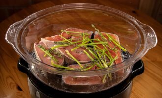 Стейки кеты кладем на первый ярус пароварки. Сверху кладём на них веточки тимьяна и оставшиеся стебли петрушки.