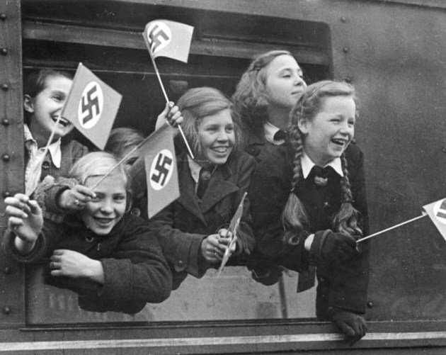 Дети машут флажками перед отъездом из Берлина, около 1940-1945 гг. 
Эти дети эвакуируются из города, чтобы жить в лагерях Kinderlandverschickung, где они будут защищены от воздушных налетов. 