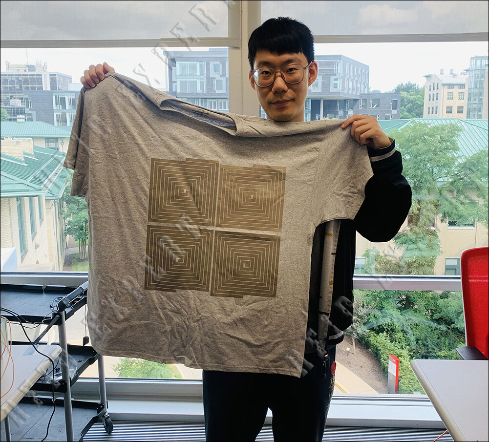 Джунбо Чжан держит рубашку с вплетенными антеннами катушки считывателя TextileSense. 