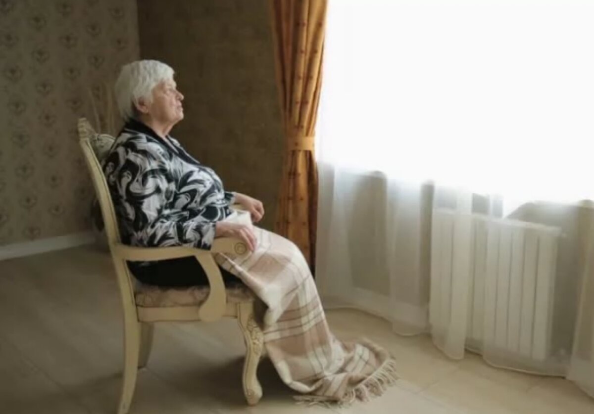 Пожилая женщина сидит у окна