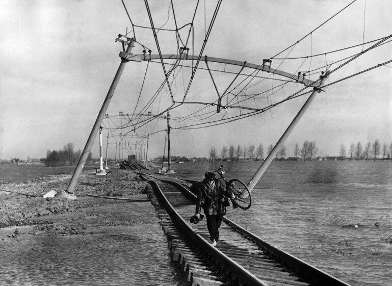 История фото 1953 года: босой мужчина несет велосипед по искореженным рельсам