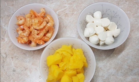 Манго очистить от кожицы и нарезать кубиками. Моцареллу мини разрезать на половинки. Креветки разморозить и обжарить на масле с чесноком 2–3 минуты.
