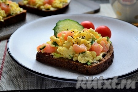 В миску разбить 2 яйца, добавить соль по вкусу и 1 столовую ложку сметаны любой жирности (или йогурта).Взбить яичную массу до однородности венчиком, добавить измельчённый зелёный лук, снова перемешать венчиком.Вылить яичную массу на сковороду, предварительно разогретую с 10 граммами сливочного масла.Жарить яйца на среднем огне, постоянно перемешивая, чтобы получился омлет кусочками.Дать омлету остыть. К омлету, по желанию, можно добавить нарезанное небольшими кусочками филе любой красной рыбы слабого соления, перемешать. Можно, конечно, к омлету и ничего не добавлять. Ломти чёрного хлеба смазать оставшимся размягчённым сливочным маслом и сверху выложить омлет. Украсить бутерброды кружочками свежего огурец.Очень вкусные и необычные бутерброды с омлетом немного посыпать сверху свежемолотым чёрным перцем и подать к завтраку или к праздничному столу.