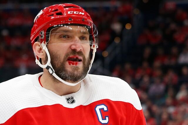 Интересный сюжет развивается в настоящее время в НХЛ. Российский форвард клуба «Вашингтон Кэпиталз» Александр Овечкин стал объектом преследования со стороны своего обиженного фаната. Нюанс в том, что фанат в настоящее время тоже является игроком НХЛ.
«Если вы не подпишете карточку, то, когда я окажусь в НХЛ, вас будет ждать очень жёсткий силовой приём»
Тринадцать лет тому назад 11-летний сын хоккеиста Рэнди Вуда Майлз написал письмо своему любимому игроку Александру Овечкину.
«Он послал хоккейную карточку Александру Овечкину. Написал он так: "Если вы не подпишете карточку и не вернёте её мне, то, когда я окажусь в НХЛ, вас будет ждать очень жёсткий силовой приём"», — рассказывал в интервью журналистам Вуд-старший.
 Александр Овечкин.
СТАТЬЯ ПО ТЕМЕ
659-й «подарок» Ови. Превзойдет ли Александр Овечкин Уэйна Гретцки?
Россиянин карточку не подписал и не вернул, и юный болельщик затаил обиду. Широко известно об этой истории стало в 2016 году, когда Майлз Вуд дебютировал в НХЛ в составе клуба «Нью-Джерси». Репортеры организовали Овечкину и Вуду встречу накануне матча их команд 30 декабря 2016 года. Россиянин пояснил, что не хотел обижать своего маленького поклонника, а разобрать всю почту, приходящую от фанатов, он просто не в состоянии. В качестве компенсации Александр подарил своему теперь уже коллеге фотографию с автографом и пожеланием: «Майлзу. Полегче сегодня!»
Вуд написал в своем Instagram: «Сегодня я буду играть против своего кумира детства. Спасибо, Александр Овечкин, великая восьмёрка!» Тот матч, кстати, закончился победой «Нью-Джерси» в серии буллитов, но ни россиянин, ни американец не сумели отличиться.«А мы-то думали, что он твой кумир»
Нападающий «Нью-Джерси» после игры рассказал журналистам: «Это потрясающе. Это очень мило с его стороны. Конечно, я смотрел на своего папу в НХЛ, но смотрел за игрой Овечкина и по-прежнему иногда смотрю, когда он делает что-то особенное. Когда я был на разминке, мы переглянулись и улыбнулись друг другу. Было приятно его видеть. Он большая личность, это я понял. Это была мечта. Я смотрел за его игрой с тех пор, когда ему было 18. Я до сих пор смотрю на его хайлайты. Было очень весело играть в овертайме 3 на 3 против него».
На этом бы истории закончиться. Но Вуд, к удивлению многих, стал целенаправленно искать возможности задеть Овечкина.
Во время встречи команд в октябре 2018 года возникла стычка, во время которой Овечкин сошелся с форвардом «Нью-Джерси» Блейком Коулманом. Но тут, в нарушение всех неписанных норм, Вуд влез в этот поединок третьим, прыгнув на россиянина со спины. Удивленный Коулман, который не собирался участвовать в драке «двое на одного», отошел в сторону, и Овечкин переключился на молодого, но дерзкого противника.
Известно, что Овечкина кулачными боями на льду не испугать. Однако полноценного поединка не получилось — оставшись с россиянином один на один, Вуд сник и драться не стал.Клюшкой в лицо
Ситуация, произошедшая во встрече, состоявшейся 16 января 2020 года, оказалась значительно хуже. На 6-й минуте встречи Вуд, отправляясь на скамейку запасных, попросту ткнул клюшкой в лицо Овечкина. На повторе видно, что американец успел посмотреть на российского игрока, а значит, весьма вероятно, что удар был умышленным. Вуд даже не обернулся в сторону упавшего Ови. Судьи этот момент, что называется, прозевали, а звезде понадобилась медицинская помощь, поскольку лицо Овечкина было в крови.Подобные атаки в НХЛ не прощают, и уже в следующей смене защитник «Вашингтона» Радко Гудас вызвал Майлза Вуда на бой, но тот уклонился от поединка. Александр не из тех парней, кого можно запугать. Уже через несколько минут после оперативного «приема у врача» он вернулся на лед, чтобы устроить «дьяволам» из Нью-Джерси настоящую взбучку.

Ответил Овечкин так, как подобает одному из лучших снайперов за 100-летнюю историю НХЛ. Уже концу первого периода он забил две шайбы, а в третьем оформил второй в сезоне и 25-й в карьере хет-трик. Теперь у россиянина 689 заброшенных шайб в регулярных чемпионатах НХЛ, и он лишь на один гол отстает от великого Марио Лемье, занимающего 10-е место в списке лучших снайперов за всю историю лиги.
«После этого я немного обезумел и сам наказал соперника»
«Вашингтон» одержал победу со счетом 5:2.
«Что я думаю о поступке Вуда? Я получил клюшкой в лицо, но свистка не последовало, — рассказал Овечкин в послематчевом интервью. Я не думаю, что это было сделано намеренно, но арбитры это не заметили. После этого я немного обезумел и сам наказал соперника, нашёл, что ответить. С самим Вудом не разговаривал».Можно констатировать, что 24-летний американец ничего, кроме вреда, своим поступком команде не принес. Да и в целом симпатии любителей хоккея к Вуду явно поубавились — откровенное хамство в отношении легенд североамериканские зрители не приветствуют. Ко всему прочему, лига может вынести дисквалификацию Майлзу на основании видеозаписи.
В общем, мальчику пора уже расстаться с детскими обидами и повзрослеть. Ибо имя Овечкина останется в истории мирового хоккея навсегда, а Майлз рискует запомниться только как «тот парень, который обижался на Ови».