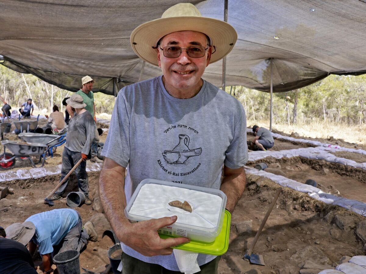    Израильский археолог Йосеф Гарфинкель показывает фрагмент керамики возрастом 3100 лет с надписью на раскопках в Хирбат-эр-Раи© AFP 2023 / MENAHEM KAHANA
