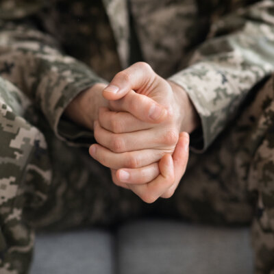    Cropped of soldier sitting on couch alone, suffering from loneliness and depression at home after returning from military service, hands of unrecognizable man in camouflage uniform, closeup Валерий