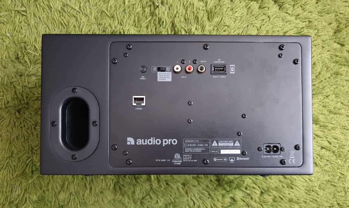 На задней панели расположен фазоинвертор, который вносит свои требования к расположению акустики. Рядом находится металлическая панель со всей электроникой. Тут есть: Ethernet, USB, выход под сабвуфер, два RCA входа,переключатель режимов воспроизведения и гнездо питания