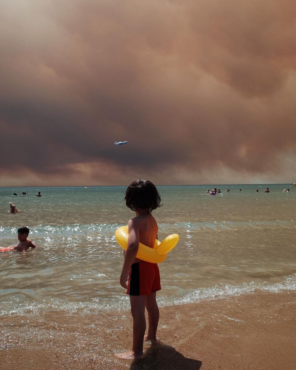 Мальчик, забывший о купании при виде пожарного самолета на фоне затянутого дымом неба над пляжем в Турции