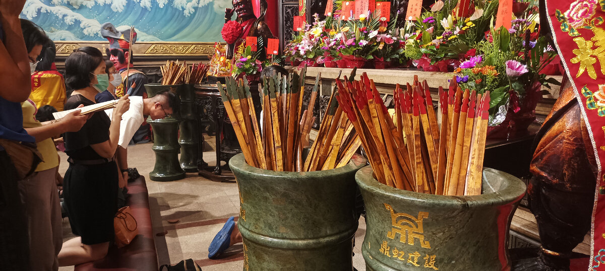 На заднем плане мужчина бросает дощечки, на переднем - ваза с палочками 