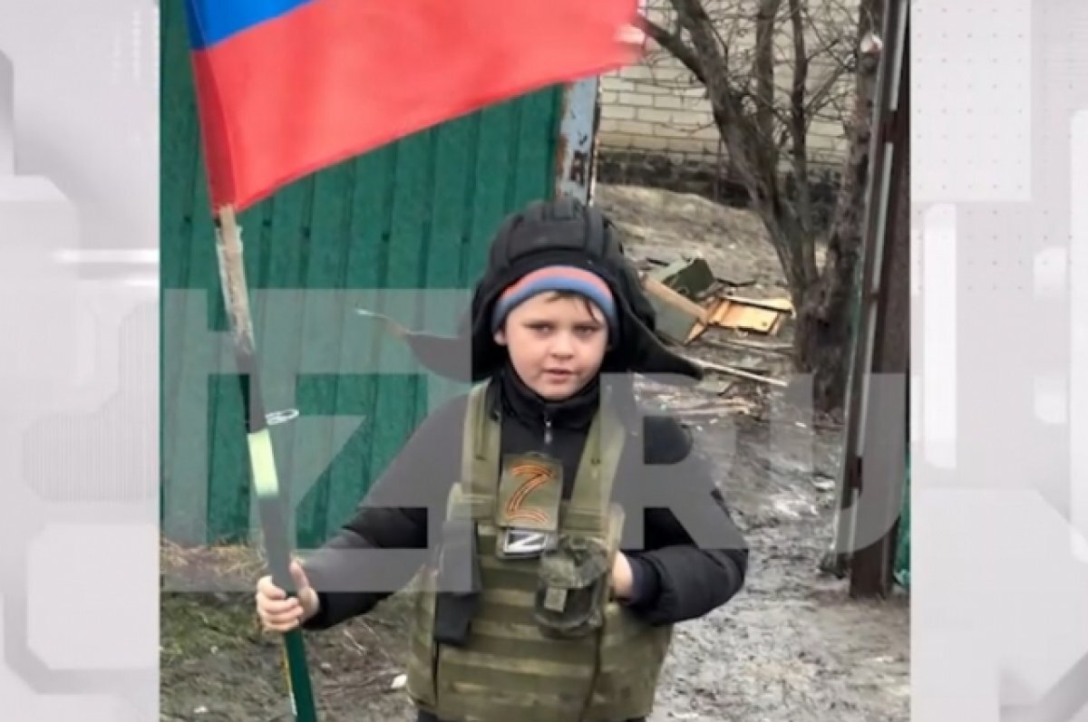    Мальчик в шлеме танкиста с флагом РФ встречает машины в ЛНР