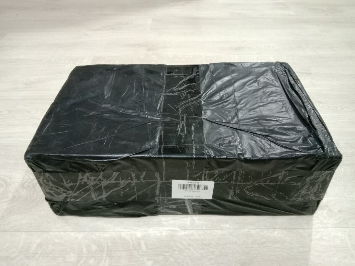 Коробка без излишеств, запакована в черный пакет.