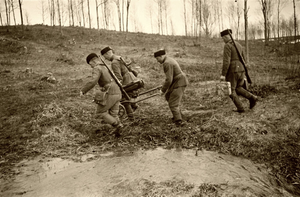 Расчет пулемета «Максим» казачьего подразделения производит переноску пулемета через топкое место в низине. Одна из патронных коробок имеет зимнюю окраску.