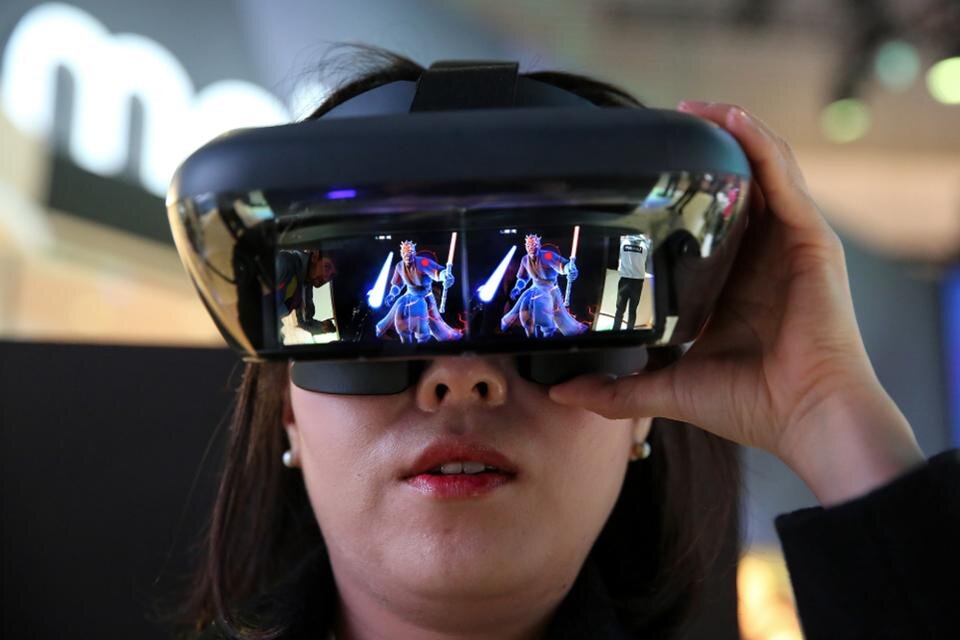 Участник MWC 2018 примеряет головную гарнитуру Lenovo с расширенной реальностью (AR) на MWC 2018 . (Фотограф: Angel Garcia / Bloomberg)