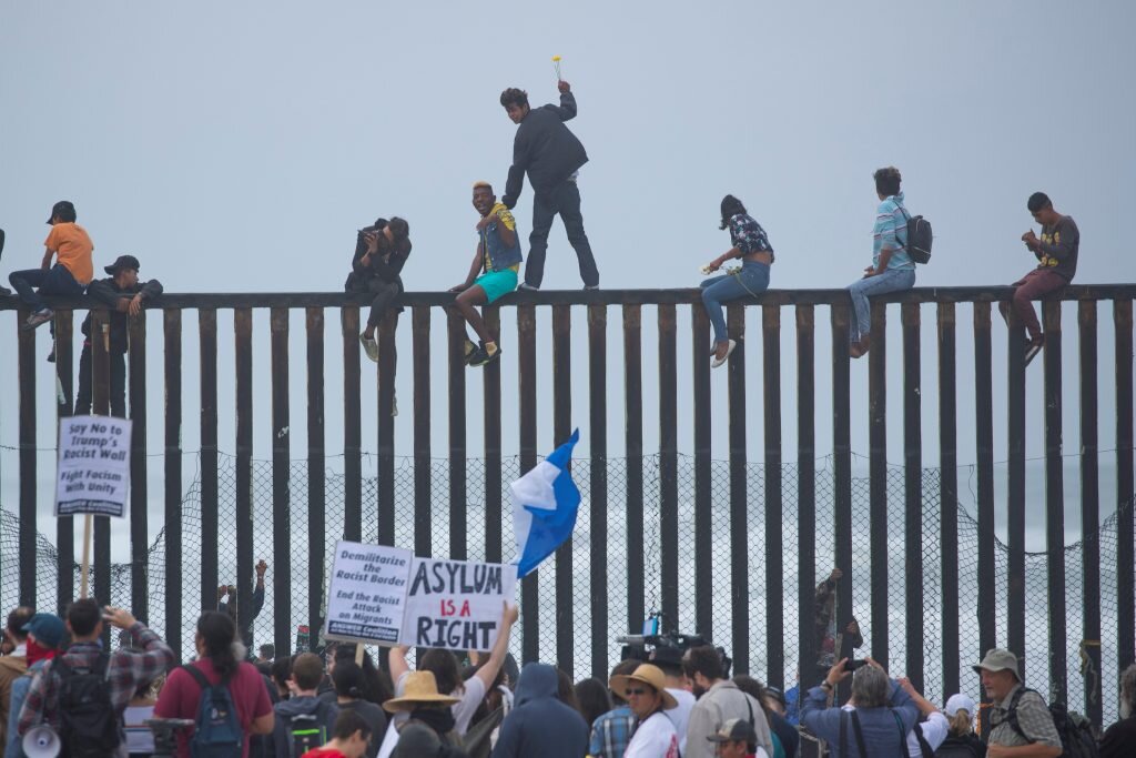 People in Mexico climb the border wall fence as a caravan of migrants and supporters reached the United States-Mexico border near San Diego, California, U.S., April 29, 2018. REUTERS/Mike Blake