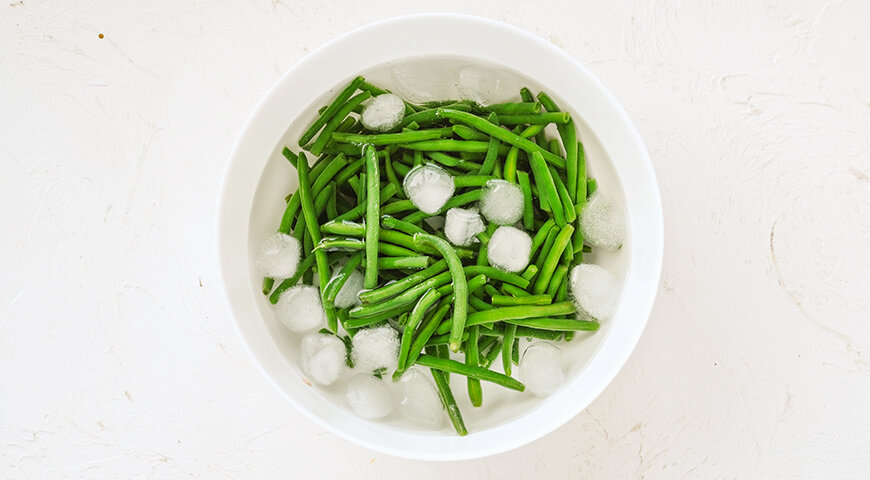 1. Начните готовить простой и вкусный салат без мяса с фасоли. И для нее заранее подготовьте миску с ледяной водой и кубиками льда.
2. Фасоль отварите в кипящей подсоленной воде 3–4 минуты, чтобы она еще оставалась хрусткой. Горячую воду слейте и немедленно опустите фасоль на 3–4 минуты в миску с ледяной водой. Затем воду слейте. Совет: если фасоль длинная, нарежьте на кусочки поменьше.