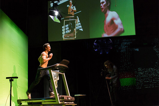 Сцена из спектакля. Экран находится наверху, но по ходу действия передвигается вверх и вниз, вперёд и назад.