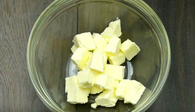 В данном рецепте предлагаем вам приготовить гренки с чесноком с добавлением сыра. За основу рекомендуем взять белый хлеб для тостов, французский хлеб или любой другой. Такие гренки вы можете приготовить и из черного хлеба, но вкус такой закуски будет совершенно другим. Итак, начнем с приготовления начинки. Для этого нарезаем кубиками сливочное масло, отправляем его в глубокую емкость и оставляем при комнатной температуре, чтобы оно размягчилось.