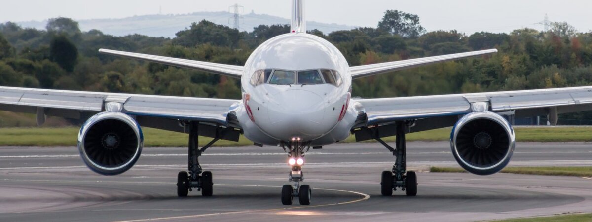 Boeing 757 выруливает на взлётно-посадочную полосу с сочной зеленью на заднем плане.