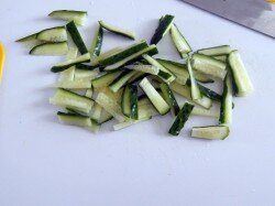 Подготовим ингредиенты для салата. Это будет обычный овощной салат из свежих овощей с копченой колбасой, сыром и чипсами, просто красиво уложен на тарелке, по цветам и форме напоминая собой радугу. Но не стоит увлекаться подборкой ингредиентов по всем цветам радуги, кроме схожести с ней, он все-таки должен быть вкусен и сочетаем по составу. Овощи тщательно моем. Огурцы нарежем тонкой соломкой.