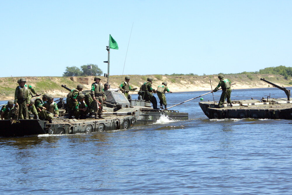 Враг начал опасно маневрировать в паре километров от позиций. Расстояние небольшое, но впереди Ока. Это почти 500 метров водной преграды. Задача – в кратчайшее время переправить на другой берег личный состав и технику. БТРы сами доплывут, но подступы к реке могут быть заминированы. На помощь пришли Инженерные войска Западного военного округа. Понтонеры этого подразделения уже несколько лет считают лучшими не только в стране, но и в мире. Соорудив понтонную переправу участок на другом берегу был проверен и разминирован. Путь свободен. По такой легенде прошли учения понтонеров на границе Нижегородской и Владимирской областей.