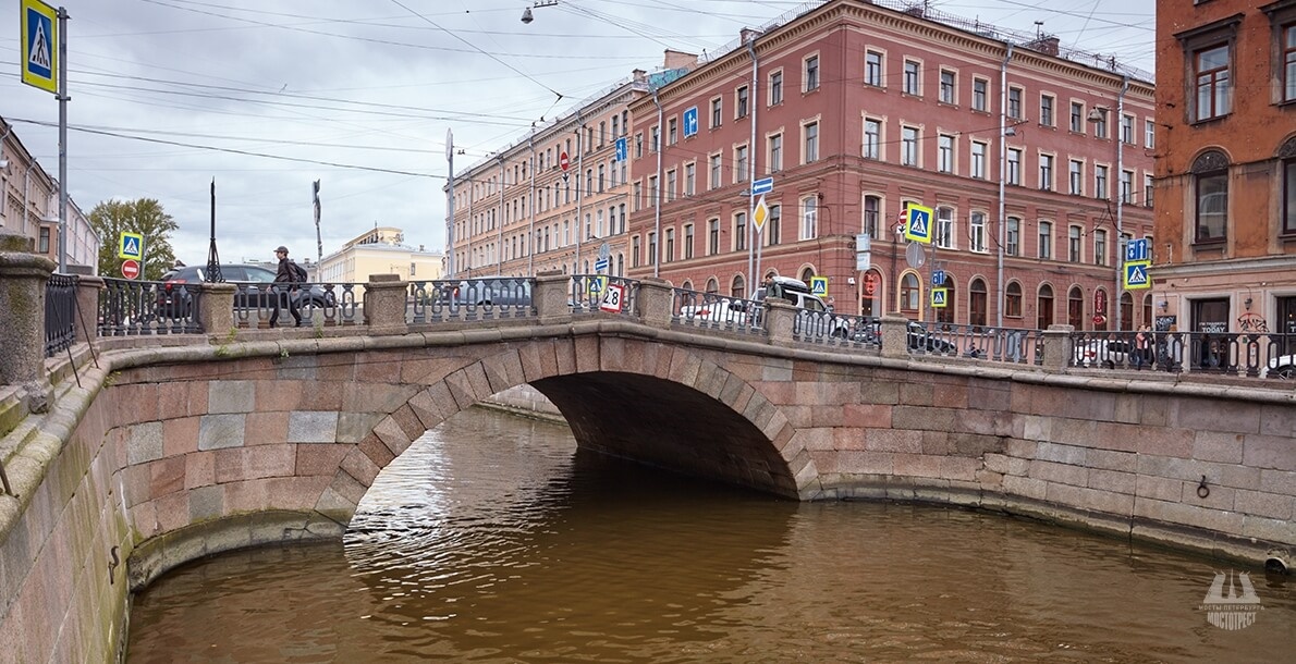 Перила моста повторяют узор перил набережной канала — чугунные балясины с массивными гранитными тумбами и металлическим поручнем. 
