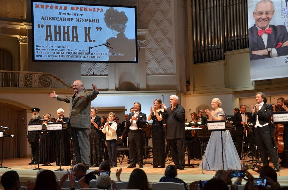 Фото: Марина Павлова

Мировая премьера оперы – событие по нынешним временам не такое уж частое. Особенно, если это так называемая гранд-опера – большая опера с полноценным сюжетом и драматургическим развитием, с обилием действующих лиц, распевающих мелодичные арии и ариозо, дуэты и ансамбли, с огромным симфоническим оркестром и внушительным хором... Попахивает анахронизмом. Особенно, если такая опера – всерьез. Сегодня, если что-то подобное и появляется в оперном жанре, то чаще как своего рода стеб, эдакое зубоскальство по поводу пафосных оперных форм и форматов – с обилием стилизаций и аллюзий на оперную музыку прошлых эпох. Именно в таком ключе были выдержаны, например, десятниковские "Дети Розенталя", написанные в 2005 году для Большого театра, или представленная в прошлом году в "Зарядье" опера Владимира Николаева "Рабочий и колхозница".

Но некоторые композиторы все же продолжают пытаться писать большие оперы всерьез. Например, Александр Журбин, празднующий в этом году знаменательный юбилей, по случаю чего он проводит в столице целый фестиваль, игриво названный им "Серьезно и легко!" И именно мировая премьера его оперы "Анна К." в Концертном зале им. Чайковского стала вторым событием этого фестиваля, который будет длиться полгода – сентября по февраль. Причем это уже пятый по счету монографический и авторский фестиваль композитора.

Но это еще не всё: на этой мировой премьере случилась чудесная встреча сразу двух фестивалей – журбинская "Анна К." была включена в программу V Фестиваля музыкальных театров России "Видеть музыку", проводимого Ассоциацией музыкальных театров России при поддержке Министерства культуры России и Фонда президентских грантов. Этот форум проходит в столице с конца сентября по начало ноября: к сожалению, его афиша претерпевает изменения в сторону сокращения в силу пандемийно-карантинных реалий сегодняшнего дня, но все же многие интересные события на нем уже состоялись или еще состоятся, и он, безусловно, невероятно разнообразит музыкально-театральную афишу Москвы.

Мировая премьера прошла в формате концертного исполнения. Хотя режиссер концертной версии Игорь Яцко пытался придать ей элементы театрализации, а Илья Рябов предложил некоторый видеоряд, призванный усилить общее впечатление, все же проект с трудом можно назвать даже semi-stage. При этом мировая премьера "Анны К." - событие театрального фестиваля: парадокс? Только отчасти: журбинская партитура насквозь пронизана театральностью, этот опус настойчиво просится именно на театральную сцену – остается только надеяться, что недалек тот день, когда опера будет поставлена в театре.

Созданная семь лет назад партитура несколько лет пролежала в Большом театре: первоначально мировая премьера планировалась именно там, в главном театре страны. Но что-то не срослось – и за ее представление "городу и миру" взялась Госкапелла Валерия Полянского, коллектив, который не боится новой музыки и нехоженых троп. Сразу вспомнилось, что восемь лет назад именно коллектив Полянского провел мировую премьеру другой оперы Журбина – "Альберта и Жизели". У Валерия Кузьмича не только мощные хор и оркестр, но и собственный пул солистов-вокалистов, а еще – огромный опыт концертных исполнений опер, как весьма популярных, так и редких, практически забытых. И, конечно же, новых.

Хотя Журбин был нацелен на создание подлинной гранд-опера, пройти мимо веяний постмодернизма, которые есть – суть культуры нашей эпохи, не под силу даже ему. Постмодернистскими по сути были и его две предыдущие оперные работы, поставленные на сценах московских театров – "Мелкий бес" и "Метаморфозы любви". В "Анне К." постмодернистский флер в стиле Акунина, Пелевина или Татьяны Толстой развернулся в полную ширь. Либреттисты Анна Родионова и Сергей Плотов оттолкнулись от великого романа Льва Толстого "Анна Каренина" и нафантазировали первый бал... нет, не Наташи Ростовой, а другой Анны Карениной – дочери толстовской героини и ее возлюбленного Вронского, которая по законам того времени и высшего света носила фамилию своего не биологического, но, если так можно выразиться, церковно-юридического отца Алексея Александровича Каренина. На этом балу юная Аннушка встречается с Вронским и узнает подлинную историю своей матери. Действие оперы разворачивается сразу в двух временных пластах – в 1893 году, когда собственно и происходит первый бал Анны-младшей, и в первой половине 1870-х, когда разворачивается жизненная драма Анны-старшей.

Таким образом, роман Толстого – это не только повод для создания оперы, но и активный участник нового опуса, мы видим на сцене хорошо знакомых персонажей классики – всех Карениных, мать и сына Вронских, Стиву Облонского, Бетси Тверскую, графиню Лидию Ивановну... Но есть и новый герой – композитор Чайковский, чью музыку слушают герои оперы и в начале 1870-х, и в 1893-м. Словом, сюжет закручен лихо и многослойно, следить за ним – увлекательно, угадывать дальнейшее развитие событий – азартно, сюжетная драматургия у новой оперы есть.  Но есть, кажется, и существенный минус: некоторая событийная избыточность, распыление внимания на множество деталей, а самое главное – качество самих текстов скорее разочаровывает. Соответствовать прозе Толстого – задача очень не простая. Похоже, либреттисты к этому и не стремись, желая сделать свое творение современным, понятным публике начала 21 века. И, кажется, здорово просчитались с этим – слушать незатейливые, простецкие, если не вульгарные фразы из уст все-таки толстовских героев несколько неуютно.

Музыка новой оперы, бесспорно, сильно выше ее либретто. В ней есть всё, что нужно для этого великого жанра, для того, чтобы поверить, что он жив и по-прежнему состоятелен – выразительные мелодии, резкие контрасты, драматургическое развитие, фактурный оркестр, музыкальные сложности и музыкальная простота, банальные, очевидные красивости, которых композитор совсем не боится, и масса ярких новаций. Есть вкусно обрисованные образы – из неглавных шикарно получились законодательница великосвестких установлений графиня Лидия Ивановна или колоритная Няня, чью партию-роль композитор поручил фольклорному голосу. Из главных – наверно, обе Анны, каждой из которых композитор дал музыку очень искреннюю. Из атмосферных – образы бала-праздника и железной дороги, красными нитями проходящие через все повествование.

Трудно с одного прослушивания объять такое гигантское сочинение: это дело будущего – тут нужен неповерхностный подход. Однако очевидно, что замысел грандиозный, и реализован он небесталанно. Немалая заслуга в этом впечатлении – у исполнителей. Прежде всего, у блистательных коллективов Госкапеллы во главе с невероятным мэтром Полянским, который уверенно совладал с непростой формой нового опуса. И, конечно же, у солистов – Екатерины Чудотворовой (Аннушка), Елены Терентьевой (Анны), Евгения Либермана (Каренин),  Андрея Бреуса (Вронский), Богдана Нагая и Максима Сажина (Сережа-мальчик и молодой Сергей), – Руслана Розырева (Стива), Юлии Томиной (Бетси), Евгении Сегенюк (Лидия Ивановна), Людмилы Кузнецовой (Вронская), Надежды Крыгиной (Няня), Валерия Гильманова (Бородатый мужик) и др., вдохнувших жизнь в героев новой русской оперы.