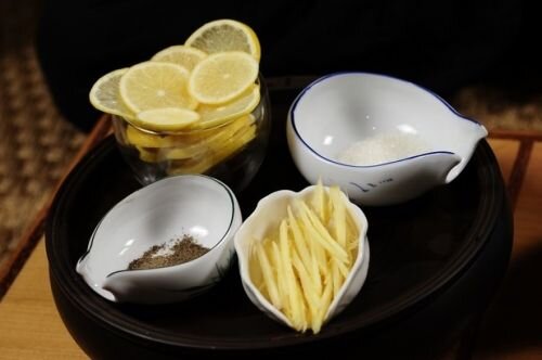     В отдельные мисочки приготовим отдельно продукты необходимые для приготовления имбирного чая. А именно нарежем тонкими дольками лимон. Мелкой соломкой нарежем корень свежего имбиря, предварительно его помыв и почистив от кожуры. Возьмем 1 щепотку молотого черного перца, и 3 столовые ложки сахара. Помните, что мёд это великолепная альтернатива сахару, и менее калорийный для соблюдающих диету.   