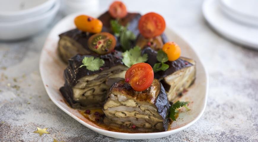 ИНГРЕДИЕНТЫ 12 крупных баклажанов
500–700 г замороженного курдючного жира одним куском
топленое масло
1 ст. л. сладкой молотой паприки
1,5 ст. л. молотой зиры
соль
зубочистки
разноцветные помидоры черри для подачи
ПОШАГОВЫЙ РЕЦЕПТ ПРИГОТОВЛЕНИЯ
Шаг 1
Замочите зубочистки в теплой воде на 1 ч. Сделайте соляной раствор из расчета 1,5 ст. л. соли на 1 л воды комнатной температуры.
Шаг 2
Нарежьте баклажаны вдоль пластами толщиной 1,5 см. Залейте рассолом, оставьте на 30 мин.
Шаг 3
Тем временем острым шефским ножом нарежьте курдюк тончайшими ломтиками. Готовые ломтики выкладывайте на лист пергамента. Посыпьте ломтики смесью зиры, паприки и 0,5 ч.л. соли.
Шаг 4
Разогрейте духовку до 180 °С. Застелите 2 противня пергаментом. Выкладывайте по 5 ломтиков баклажанов, стряхивая воду, друг на друга, прослаивая курдюком. Верхний слой (баклажан)смазывайте топленым маслом. До этого этапа все можно приготовить заранее, за 4–12 ч.
Шаг 5
Проткните каждый баклажан вертикально зубочистками через каждые примерно 6 см. Запекайте в духовке 30 мин. Перед подачей на верхний конец зубочистки наколите половинку черри и нарежьте слоеные баклажаны поперек, разрезая по середине между шпажками. Подавайте очень горячими.