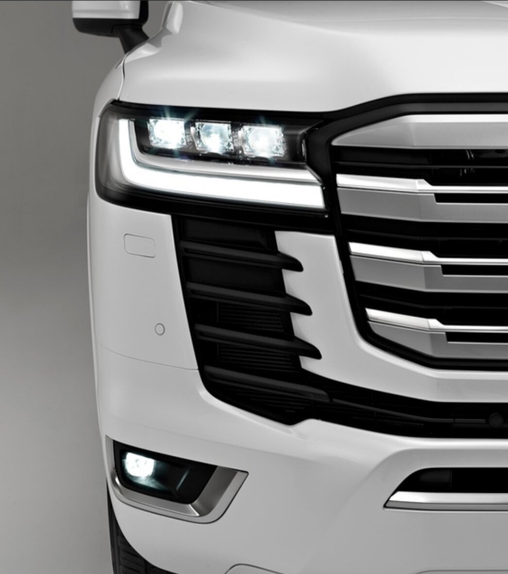 Начиная с базовой комплектации передняя оптика будет полностью светодиодной, но на выбор предоставят несколько версий. Так в базовом варианте Toyota Land Cruiser 300 установят рефлекторные фары, хотя в 200-ом все было на линзах даже в базе. Что касается максимальной комплектации Toyota Land Cruiser 300, то здесь оптика будет матричной и адаптивной. Подчеркивает оптика снизу L-образные LED ходовые огни, которые в свою очередь так же выполняют роль указателей поворотов.

Интересным моментом будут передние воздуховоды под оптикой. Именно они будут указывать на комплектацию Toyota Land Cruiser 300, а так же двигатель под капотом внедорожника. Многие уже отметили, что новый LC300 выглядит не так устрашающе, как 200-ый или генерации пораньше. В остальном же новому ЛК300 достался тот же капот, с выемкой по центру, будто дерево упало, острые линии от решетки и до передних стоек и фирменная эмблема по центру решетки радиатора.