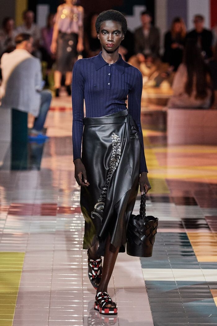 Образ от Prada объединяет роскошь и кэжуал. Длинная юбка ниспадает красивыми складками, её украшает необычный принт.