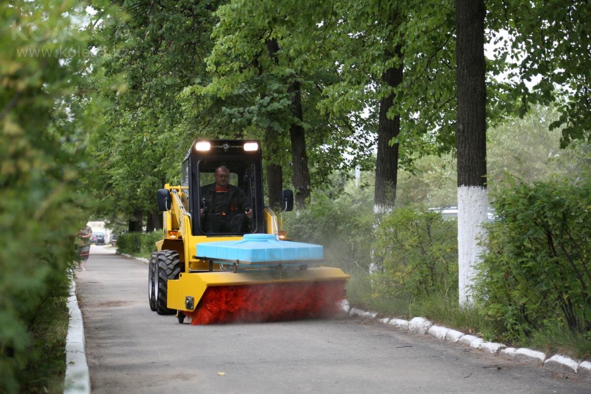 Фронтальный мини погрузчик убирает мусор с дороги коммунальной щеткой