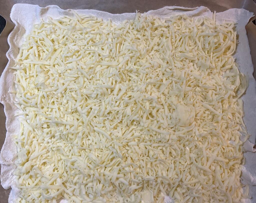 Раскатать готовое тесто-для первого слоя пирога.Трём сыр моцарелла-хорошо засыпать тесто сыром.