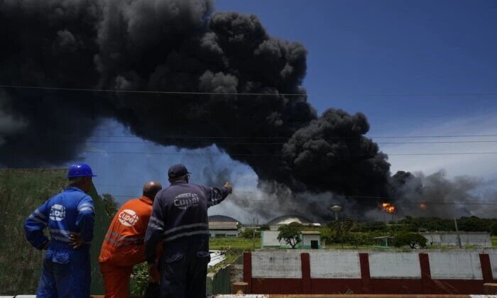 Работники Кубинского нефтяного союза, известного под испанской аббревиатурой CUPET, наблюдают за огромным поднимающимся шлейфом дыма от базы супертанкеров, пока пожарные работают над тушением пожара, начавшегося накануне вечером во время грозы, в Матансасе, Куба, 6 августа 2022 года. (Ramon Espinosa/AP Photo)