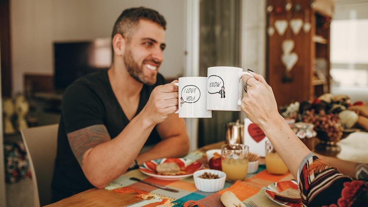    Большие кофейные чашки в руках у улыбающегося мужчины и сидящей напротив женщины:Pexels