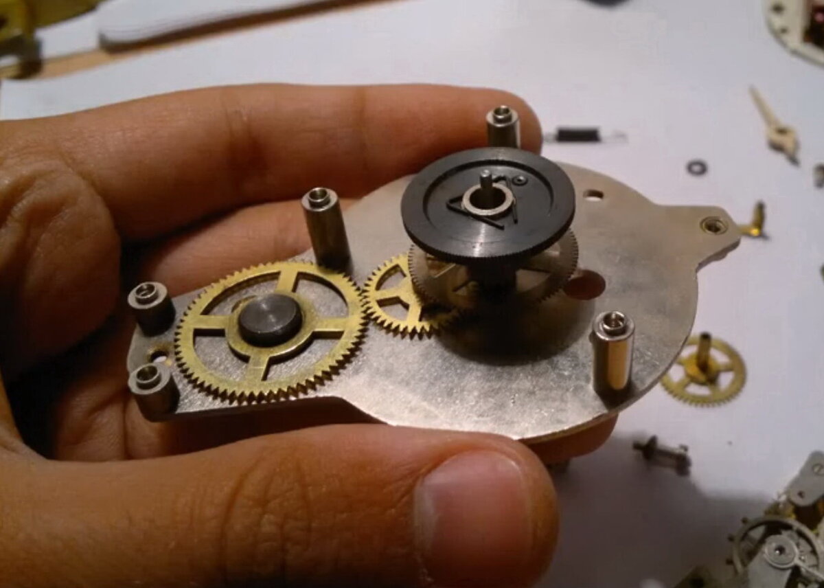 Нижняя платина . В центре внизу минутное колесо ось которого выходит на лицевую сторону. Выше его тяговое колесо. А ниже рядом ещё два колеса вексельное и промежуточное для колеса установки времени, которое закреплено на конце тросика и его ось входит в отверстие рядом. Фото из коллекции Яндекс.