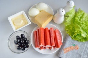 Отварите яйца, остудите и очистите от скорлупы. Крабовые палочки освободите от целлофановых пакетиков. Оливки процедите от жидкости.