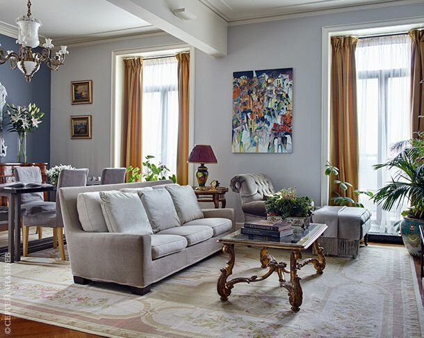 В гостиной диван, Flexform, антикварный столик из Италии. У окна сделанная на заказ кушетка в обивке из ткани Loro Piana. На дальнем плане антикварная лампа, Россия, XIX век. На стенах картины Вячеслава Кубарева и копия работы Аристарха Лентулова. На полу из дубового паркета — французский ковер-гобелен.